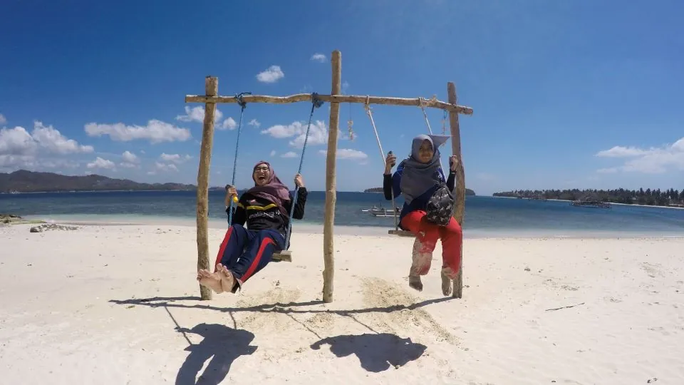 Wisatawan sedang bermain ayunan di pantai Gili Kedis dalam Paket Tour Harian Lombok